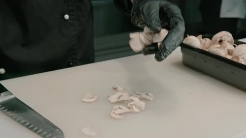 Close-up of a sushi maker in gloves cutting a mushroom on a white board in a professional kitchen
