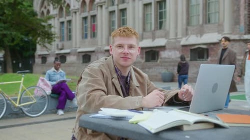 Young Student Doing Homework and Posing for Camera Outdoors on Campus