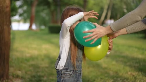 Little Girl Receives Balloons in a Green Park