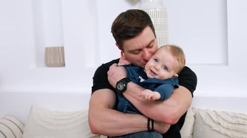 Man Holds and Kisses Smiling Infant Indoors