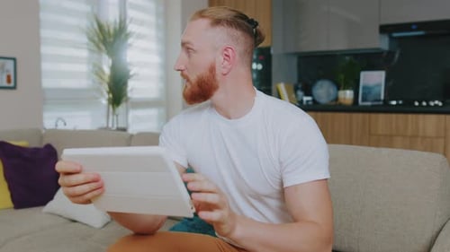 Man using a tablet sitting on a couch indoors