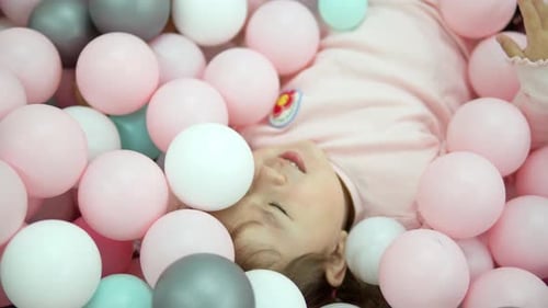 Happy Little Girl Dreamer Lying in Dry Pool With Colorful Balls Smiling
