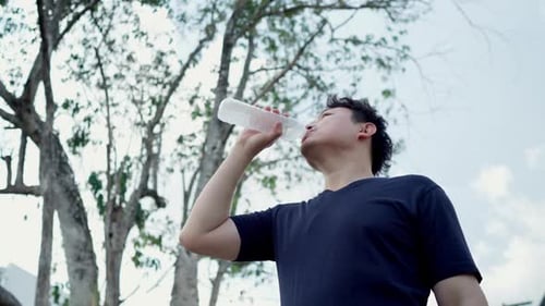 Man drinking water from a plastic bottle water after workout in forest