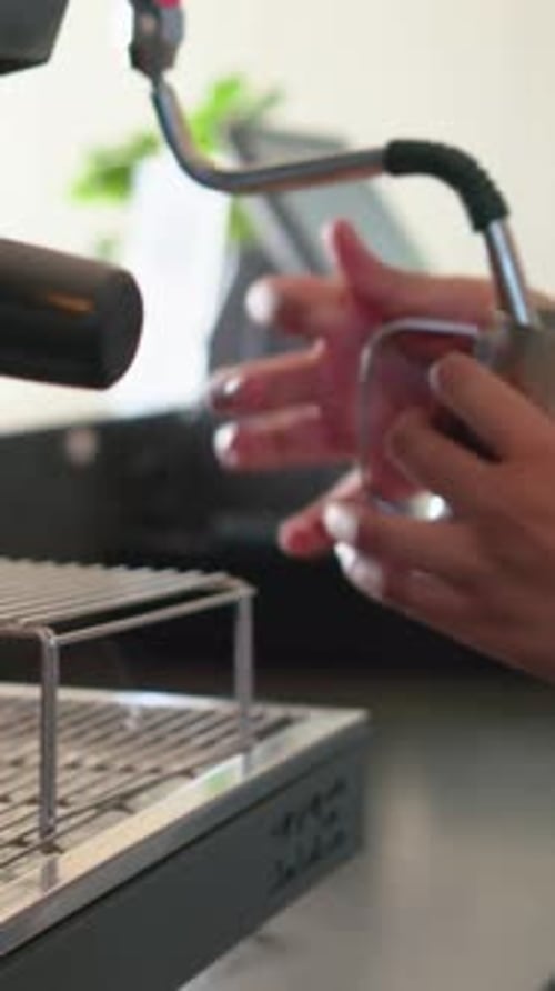 Vertical video: Placing pitcher under wand, pink band hands frothing, placing red cup at counter