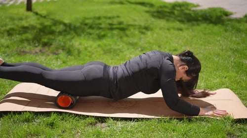 A Woman in a Gym Suit Uses a Massage Roll During a Yoga Training A Woman Performs an Exercise From