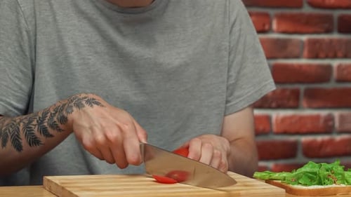 Man Prepares Sandwich With Tomato on Cutting Board