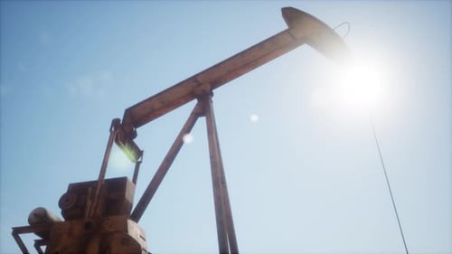Oil Pumpjack Works Against Clear Blue Sky In Remote Location