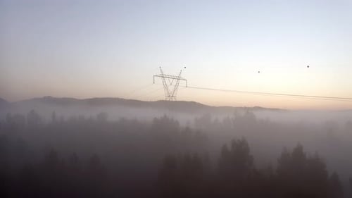 Aerial ascending shot of an electricity tower over a foggy forest.