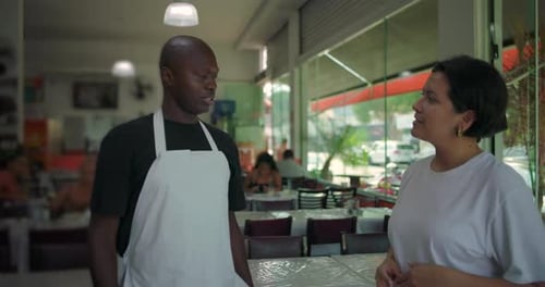 African American restaurant staff talking with female manager inside casual dining area, both