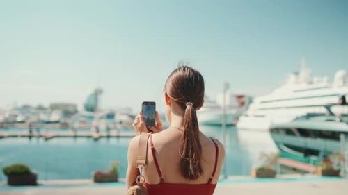 Young woman takes photos, videos of the seaport on a mobile phone