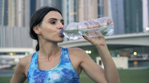 Tired Female Jogger Taking Break and Drinking Water in City 30s