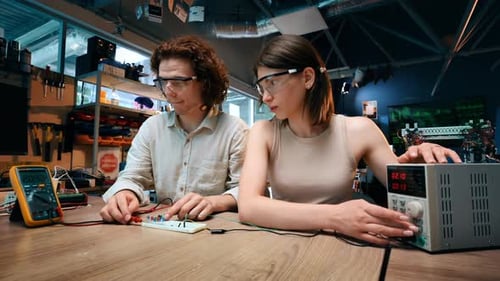 Young man and woman in protective glasses doing experiments with electricity in a laboratory. Tools