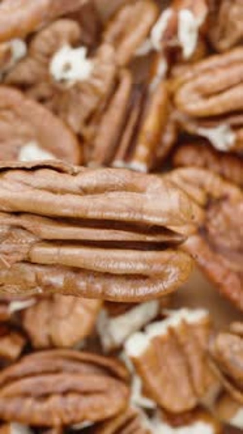 Vertical video. Slider shot. Pecan nut rotating against the background of peeled nuts, top view.