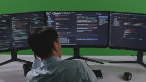 Back View Of Bored Asian Man Developer Write Code With Multiple Computer Screens In Green Screen