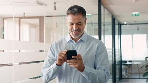Smiling Older Business Man Executive Standing in Office Using Mobile Phone