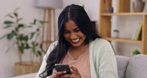 Woman Laughing While Using Smartphone on Couch Indoors