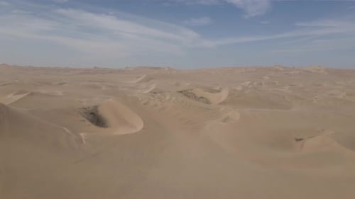 Aerial: Endless tract of desert sand dunes under wispy cloud sky