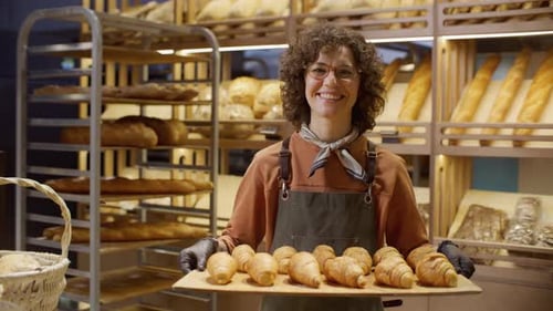 Smiling Baker Holding Tray of Fresh Croissants