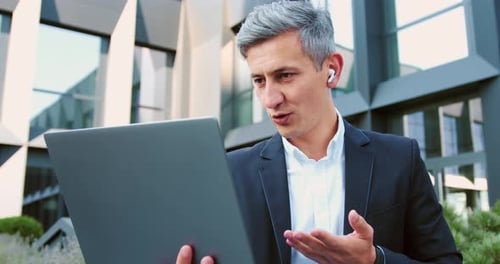 Businessman using smartphone outdoors standing on city street, smiling looking to mobile phone scree