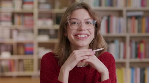 A young beautiful female student smiles into the camera while learning in the library—close-up shot.