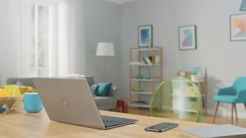 Rotating Shot of a Modern Silver Laptop on a Wooden Table at Home. Smartphone Lies on a Table Next
