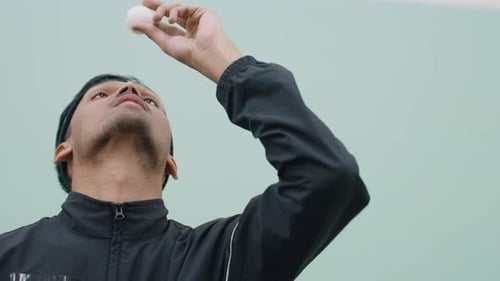 Jeune homme riant tout en équilibrant une balle de tennis en l'air