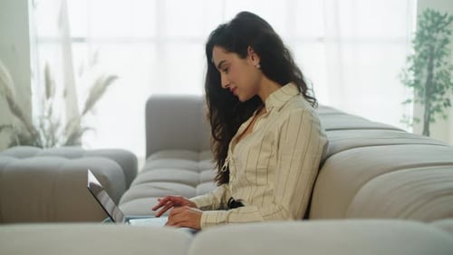 Woman Using Laptop on Sofa in Bright Living Room