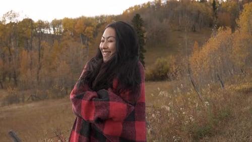De una mujer envuelta en una manta frente al bosque