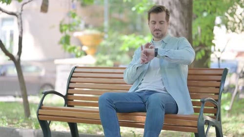 Man Sits on Bench Using Smartwatch