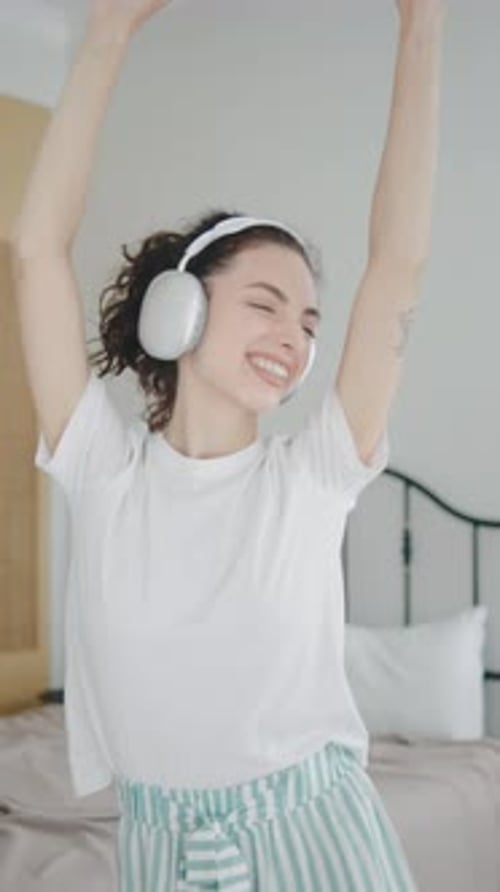 Woman Joyfully Dancing with Headphones in Bedroom