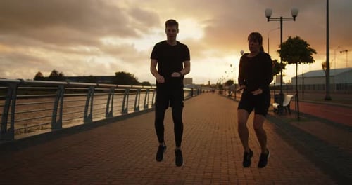 Young Man and Woman Training on the Embankment Near in the City at Sunset