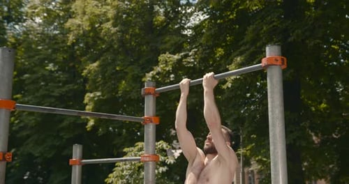 Young Man Doing Pull Ups on a Bar in the Park