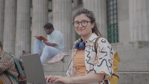 Portrait of Smiling Female Student with Laptop on Stairs Outside of University