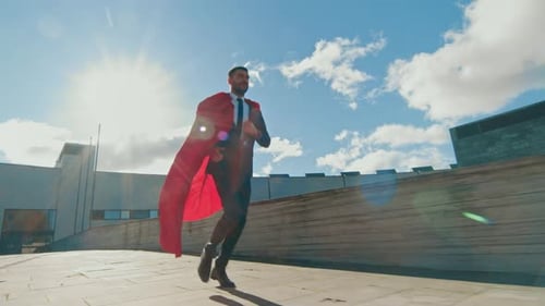 Businessman Superman WIth Red Cape Blowing in the Wind Runs on the Roof of a Skyscraper, Ready to S
