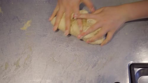 Close up shot of a child's hands kneading bread dough on an aluminum kitchen surface.