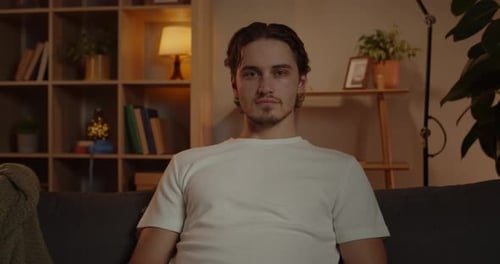 Portrait of Serious Young Man Looking to Camera Sitting on the Sofa at Living Room