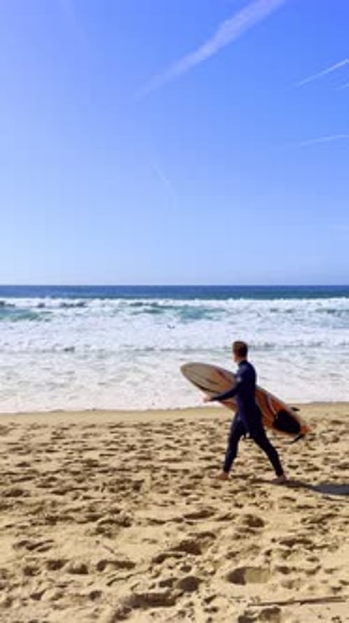 A Surfer Walking on Sunny Day on Sandy Beach Starting at Ocean Tide