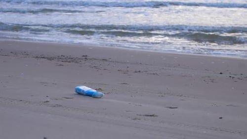 Blue plastic bottle on the beach, trash and waste litter on an empty Baltic sea white sand beach, en