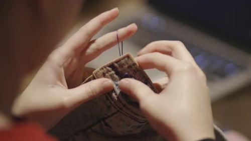 A Woman With A Tattoo Sewing A Piece Of Button On A Faded Jeans. -close up shot