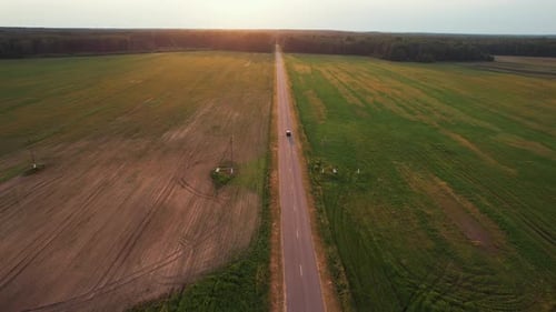 Aerial View of a Car on a Suburban Road Between Fields and a Forest on the Horizon on a Sunny Summer