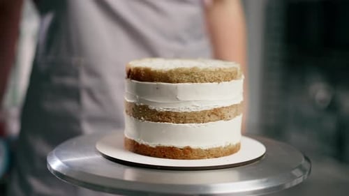 Close Up Female Baker in a Professional Kitchen Puts Blue Cream From Pastry Bag Onto a Sponge Cake