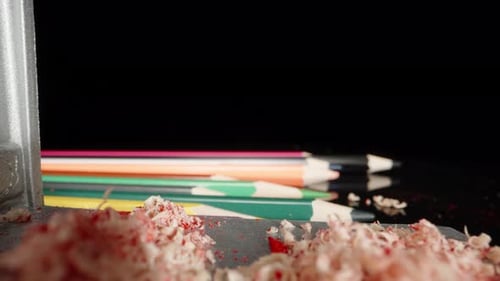 Multi-colored pencils on the table, pencil sharpener, shavings. Dolly slider extreme close-up.