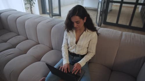 Woman working on laptop sitting on couch indoors