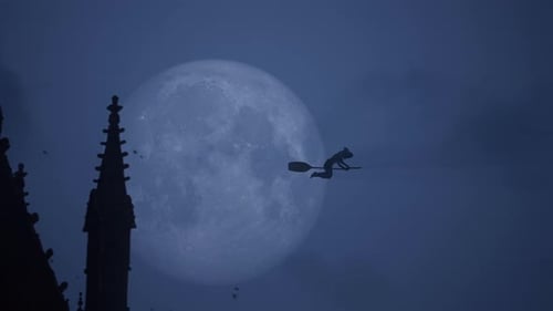 Halloween Horror Night: Witch Flying Across the Sky on a Full Moon above Gothic Cathedral Silhouette