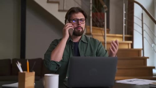 Man Talking on Phone While Working on Laptop