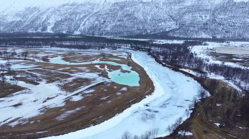 Breathtaking Aerial View of Icy River Winding Through Snowy Mountains