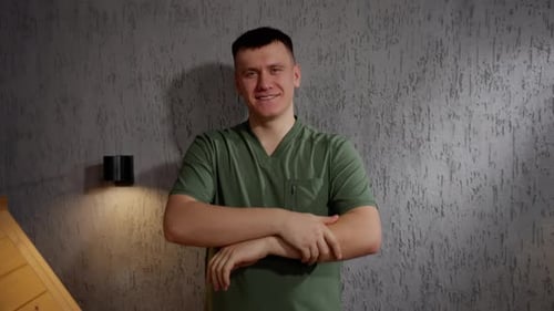 An Adult Man in a Green Shirt Stands Against a Wall His Smile Lighting Up the Indoor Space As He