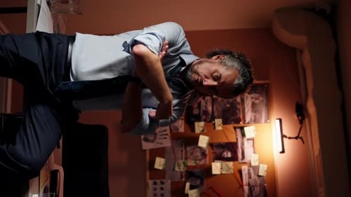 Vertical Video in the Detective's Office Middleaged Investigator in a Shirt and Tie Sits on a Table