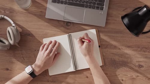 Top Down View of a Woman's Hands Writing the Title PEACE in Notebook and Drawing Icon