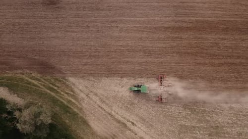 Aerial top view of tractor cutting furrows in farm field for sowing farm tractor with rotary harrow